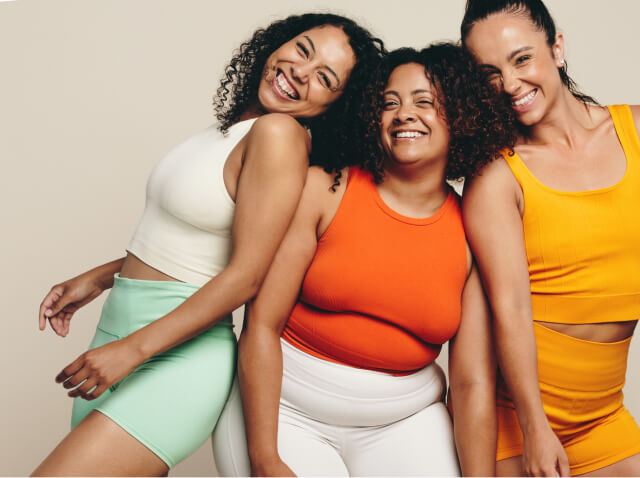 Three women wearing workout clothes smile and pose