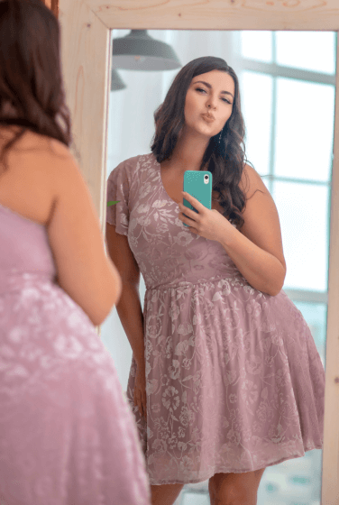 A woman in a pink dress takes a mirror selfie with a kissy face