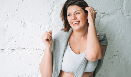 A woman smiles and fixes her hair next to the white wall